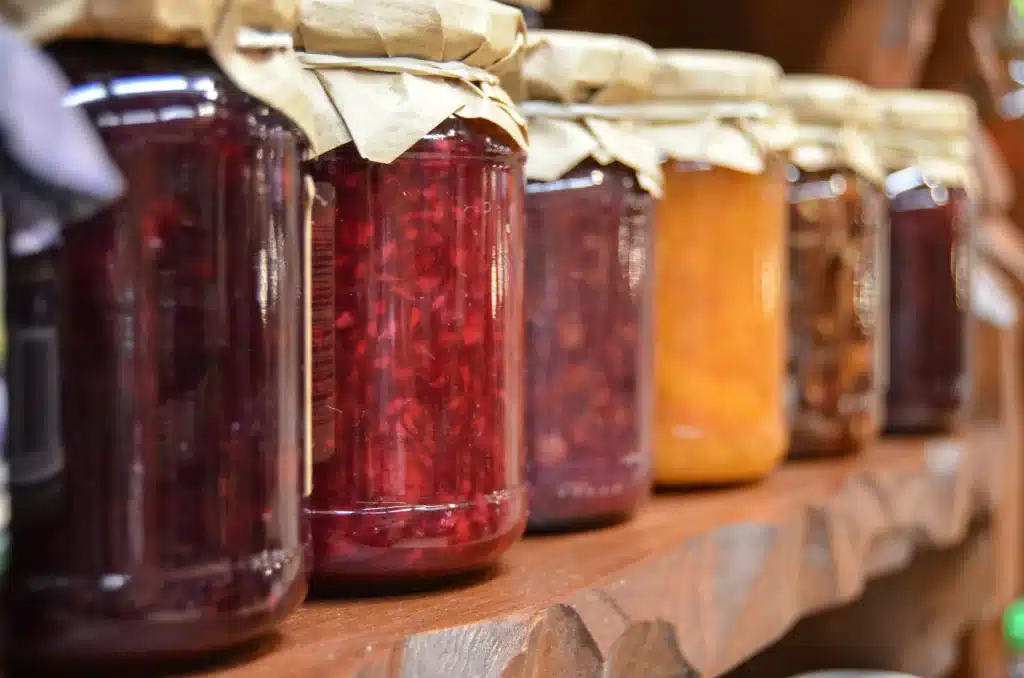 A row of homemade preserves in glass mason jars with rustic paper lids, lined up on a wooden shelf, showcasing vibrant colors of pickles and jams for page About Me
