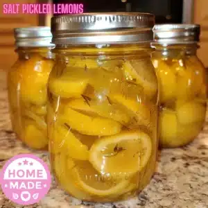 A close-up of glass jars filled with Salt Pickled Lemons, sliced and packed in brine, sealed in mason jars on a kitchen countertop.